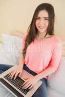 Cheerful girl looking at camera using a laptop sitting on a bed