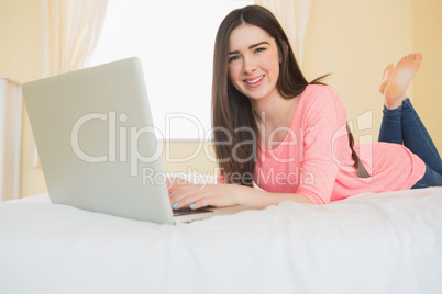 Pretty girl looking at camera using a laptop lying on a bed