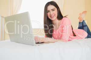 Pretty girl looking at camera using a laptop lying on a bed