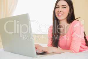 Pretty young girl looking at camera using a laptop lying on a be