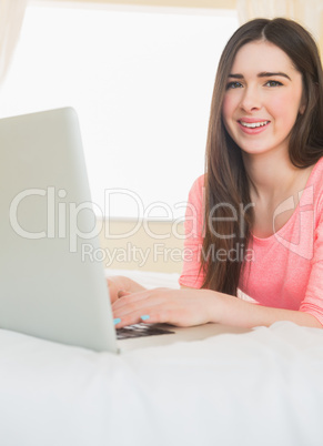 Young girl looking at camera using a laptop lying on a bed