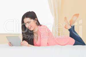 Smiling girl looking and using a tablet pc laying on a bed