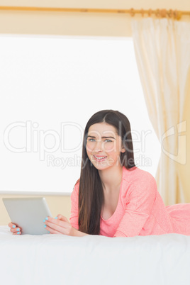 Pretty smiling girl looking at camera and using a tablet pc layi