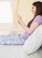 Happy girl sitting on a bed looking and using a tablet pc