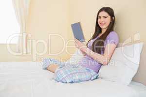 Smiling girl looking at camera and sitting on a bed reading a bo