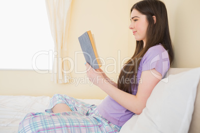 Smiling girl sitting on a bed reading a book Smiling girl sitting on a bed reading a book
