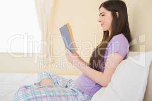 Smiling girl sitting on a bed reading a book