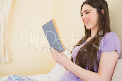Happy girl sitting on a bed reading a book Happy girl sitting on a bed reading a book