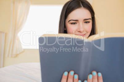 Relaxed girl lying on a bed reading a book