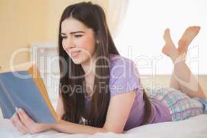 Pretty young girl lying on a bed reading a book