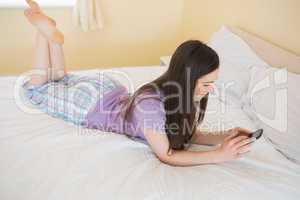 Concentrated girl lying on a bed using a mobile phone