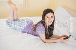 Smiling girl looking at camera and lying on a bed using a mobile