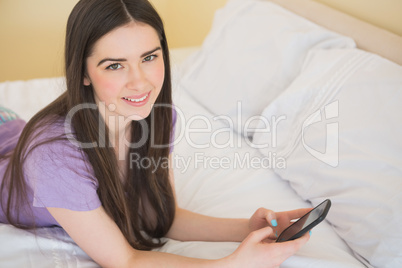 Happy girl looking at camera and lying on a bed using a mobile p