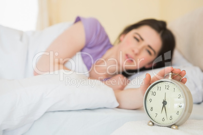 Upset girl in her bed turning off her alarm clock