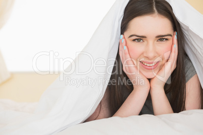 Happy girl looking at camera lying in her bed