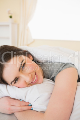 Smiling brunette relaxing in her bed