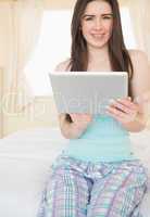 Cheerful girl looking at camera and using a tablet pc sitting on