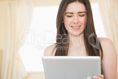 Content girl using a tablet pc sitting on her bed