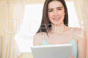 Smiling young woman looking at camera and using a tablet pc sitt
