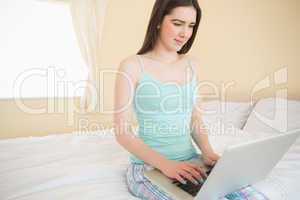 Smiling girl using a laptop sitting on her bed