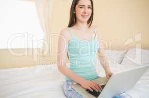 Smiling girl looking at camera and using a laptop sitting on her