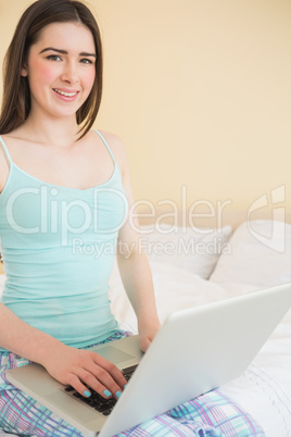 Happy girl looking at camera and using a laptop sitting on her b