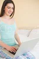 Happy girl using a laptop sitting on her bed