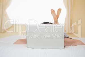Girl lying on a bed hiding behind a laptop