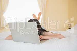 Girl on a bed hiding behind a laptop