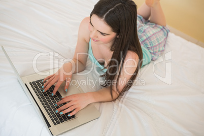 Brunette girl lying on a bed using a laptop