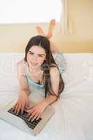 Young girl looking at camera and lying on a bed using a laptop