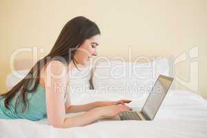Content young girl lying on a bed using a laptop