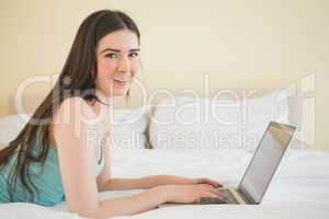 Content girl looking at camera using a laptop lying on a bed