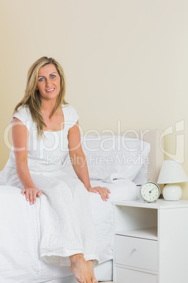 Pleased woman looking at camera and sitting on a bed