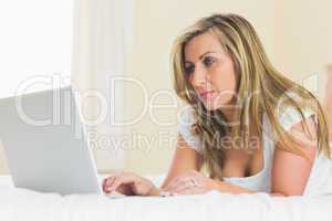 Concentrated woman using her laptop lying on her bed