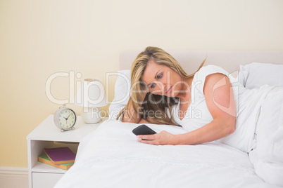 Concentrated woman using a mobile phone lying on her bed