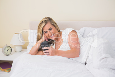 Happy woman texting on her mobile phone and lying on her bed