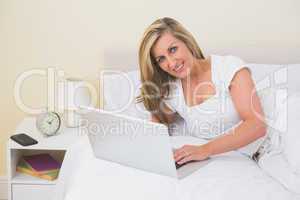 Pleased woman using a laptop lying on her bed