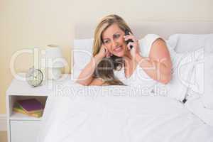 Smiling woman lying on a bed calling someone with her mobile pho