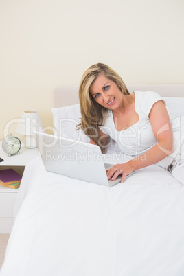 Content woman using a laptop lying on her bed