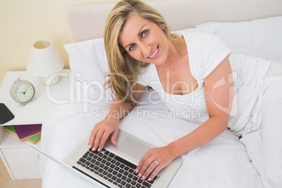 Happy woman using a laptop lying on her bed