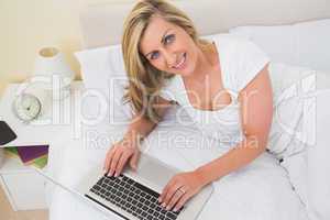 Happy woman using a laptop lying on her bed