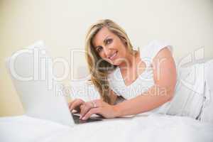 Cheerful woman typing on a laptop lying on her bed