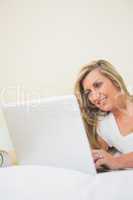 Happy woman typing on a laptop lying on her bed