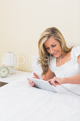 Content woman using a tablet pc lying on her bed