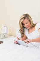 Content woman using a tablet pc lying on her bed