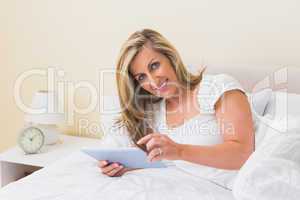 Pleased woman using a tablet pc lying on her bed