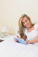 Amused woman using a tablet pc lying on her bed