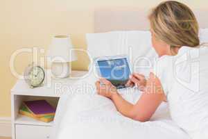 Concentrated woman using a tablet pc lying on her bed
