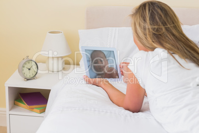 Focused woman using a tablet pc lying on her bed